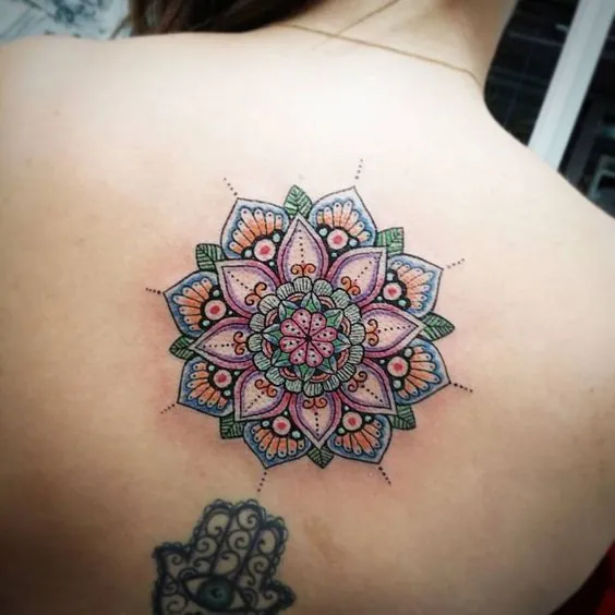 Colour mandala tattoo on the upper back with a small hamsa hand below